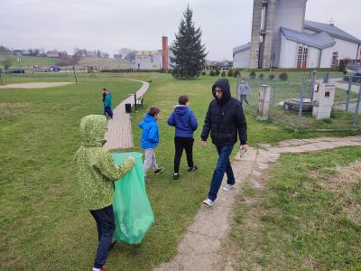 Uczniowie sprzątaja otoczenia ławy ze śmieci. podnoszone są śmieci, które są zbierane do zielonych worków.