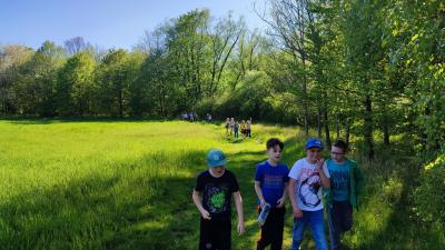 Grupa dzieci wraz z rodzicami w drodze powrotnej z cmentarza wojennego. Piękna słoneczna pogoda. Uczniowie przechodzą przez łąkę.
