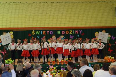 Przedszkolaki z grupy Biedronki występują na scenie - w tle napis święto rodziny. Przed sceną pięknie udekorowane kwiaty w doniczkach.