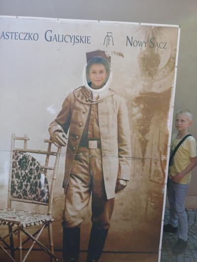Chłopiec pozuje do zdjęcia na tle planszy z postacią mężczyzny XIX wiecznego Miasteczka Galicyjskiego w Nowym Sączu