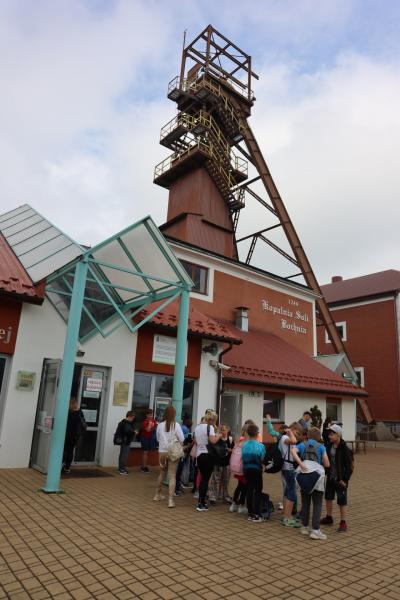Dzieci przed wejściem do budynku kopalni soli w Bochni. W tle wysoki ceglany  komin oraz wieża szybowa.