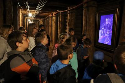 Dzieci oglądają multimedialny materiał. Wszyscy stoją w korytarzu kopalni.
