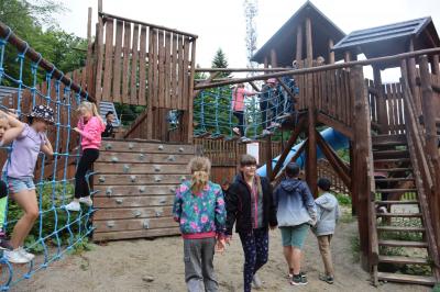 Dzieci bawia sie na dużym placu zabaw. Plac zbudowany z drewnianych pali i sznurów.