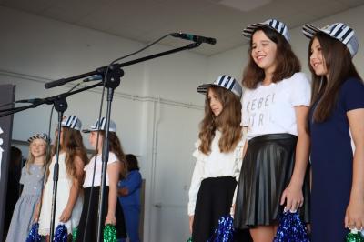 Dziewczynki klas trzecich śpiewaja do mikrofonu piosenkę. Dziewczynki mają na głowie czapeczki