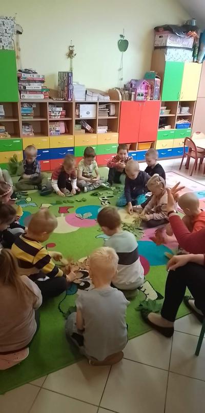 Dzieci siedzą w kole. Na dywanie przed nimi rozłożone są  liście z różnych gatunków drzew. Nauczyciel pokazuje trzy palce sugerując ile liści każde dziecko ma wziąć do ręki.