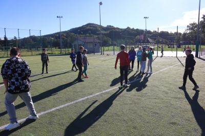 Uczniowie na boisku grają w piłkę nożną. Gra odbywa się na orliku.