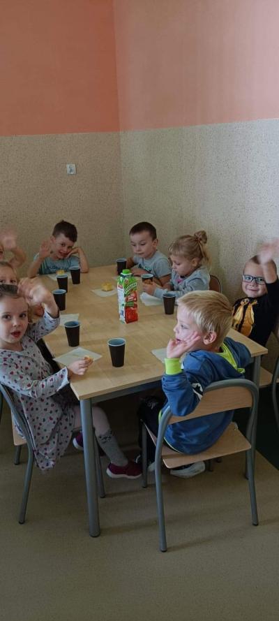 Dzieci siedzą przy stoliku, piją sok jabłkowy