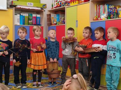 Dzieci stoją w półkolu, w rękach trzymają różne  dary jesieni