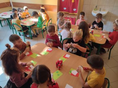 Dzieci siedzą przy trzech stolikach, wycinają kolorowe kartki.