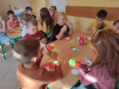 Dzieci siedzą przy trzech stolikach, wycinają kolorowe kartki