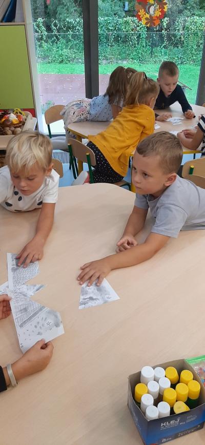 Dwóch chłopców układa puzzle przy stoliku. w tle inna dzieci z grupy Skrzaty.