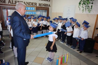Dyrektor  i wicedyrektor szkoły pasuja na ucznia dzieci z klas pierwszych. Dyrektor trzyma w ręku duży ołówek.