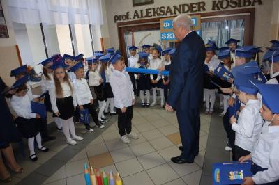 Dyrektor  i wicedyrektor szkoły pasuja na ucznia dzieci z klas pierwszych. Dyrektor trzyma w ręku duży ołówek.