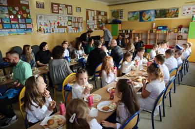 Rodzice wraz z dziećmi i wychowawcą spożywają posiłek przygotowany po uriczystości pasowania na ucznia.