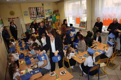 Rodzice wraz z dziećmi i wychowawcą spożywają posiłek przygotowany po uriczystości pasowania na ucznia.