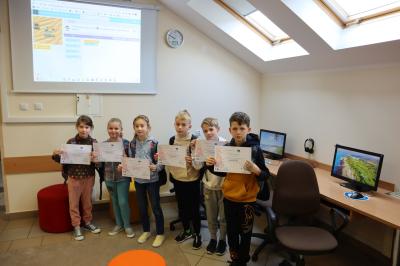 Uczniowie szkoły podstawowej pozują do zdjęcia grupowego trzymając w ręku certyfiakt uczestnictwa w codeweek 2022.