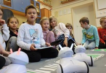 Uczeń steruje robotem photonem. 3 roboty poruszają się na macie edukacyjnej w kształcie miasta.