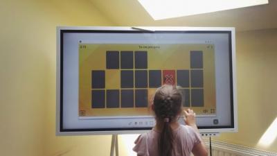 Dziewczynka gra w interaktywnym programie na monitorze dotykowym.