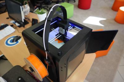 Drukarka 3D podczas wydruku modelu. Załadowany pomarańczowy filament.