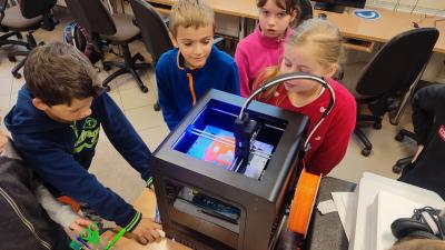 Uczniowie obserwują wydruk modelu w drukarce 3D. Na pierwszym planie drukarka Zoltrax drukująca model.