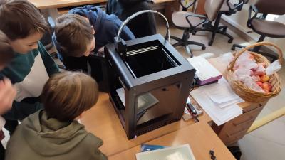 Uczniowie obserwują wydruk modelu w drukarce 3D. Na pierwszym planie drukarka Zoltrax drukująca model.