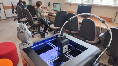 Uczniowie projektują model 3D na platformie Tinkercad. Na ekranach widać przestrzenny model bryły. Na pierwszym planie drukarka 3D oraz wydrukowana sowa.