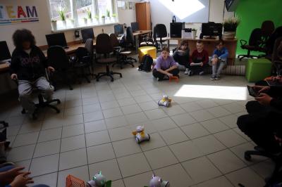 Uczniowie klasy VIb uczestniczą w zajęciach robotyki. Na podłodze roboty sterowane przez uczniów rozgrywają mecz piłki nożnej