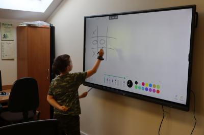 Dzieci z pomocą monitora interaktywnego ćwiczą wszystkie możliwe ruchy w grę kółko i krzyżyk podczas zajęć kończonych warsztaty związane ze sztuczną inteligencją.