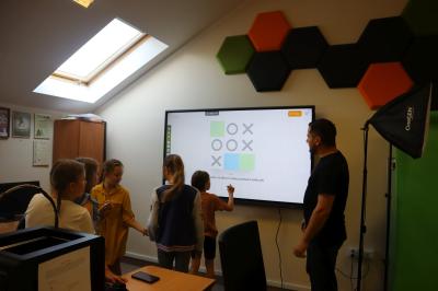 Dzieci z pomocą monitora interaktywnego ćwiczą wszystkie możliwe ruchy w grę kółko i krzyżyk podczas zajęć kończonych warsztaty związane ze sztuczną inteligencją.