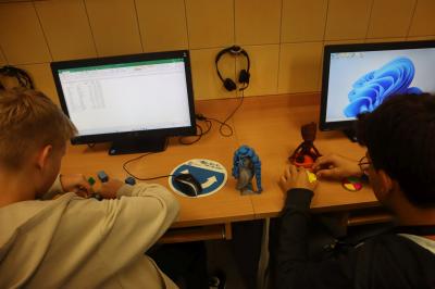 Uczniowie oglądają różne kolorowe  modele 3D wydrukowane na drukarce.