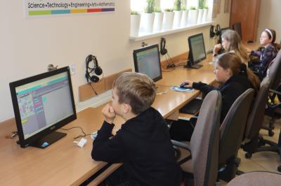 Uczniowie siedzą przy komputerach, uczą się programowania na stronie code.org.