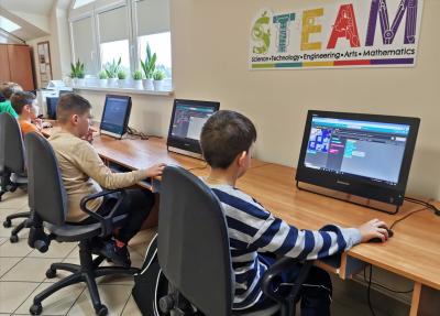 Chłopcy siedzą przy komputerach i uczestniczą w zajęciach z kodowania